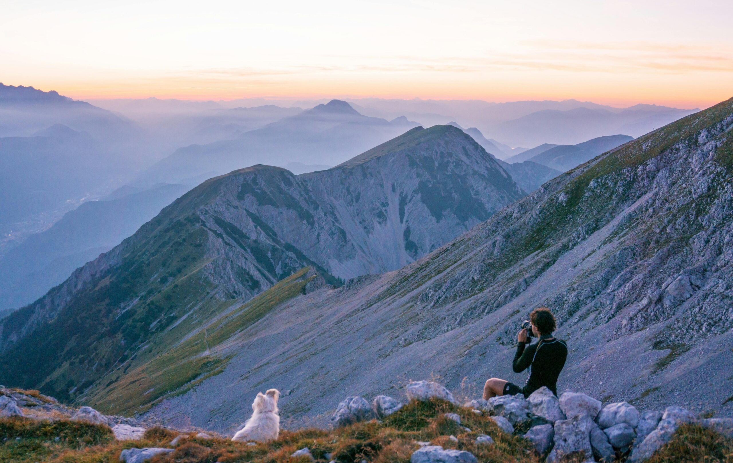 A hiker captures the serene sunrise over Slovenian mountains, with a dog by his side.